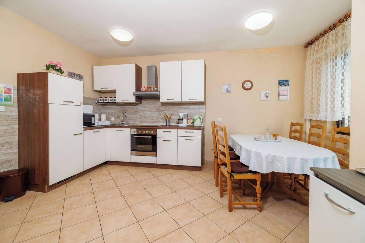 Une cuisine avec des meubles blancs, une table à manger avec des chaises et un sol carrelé.