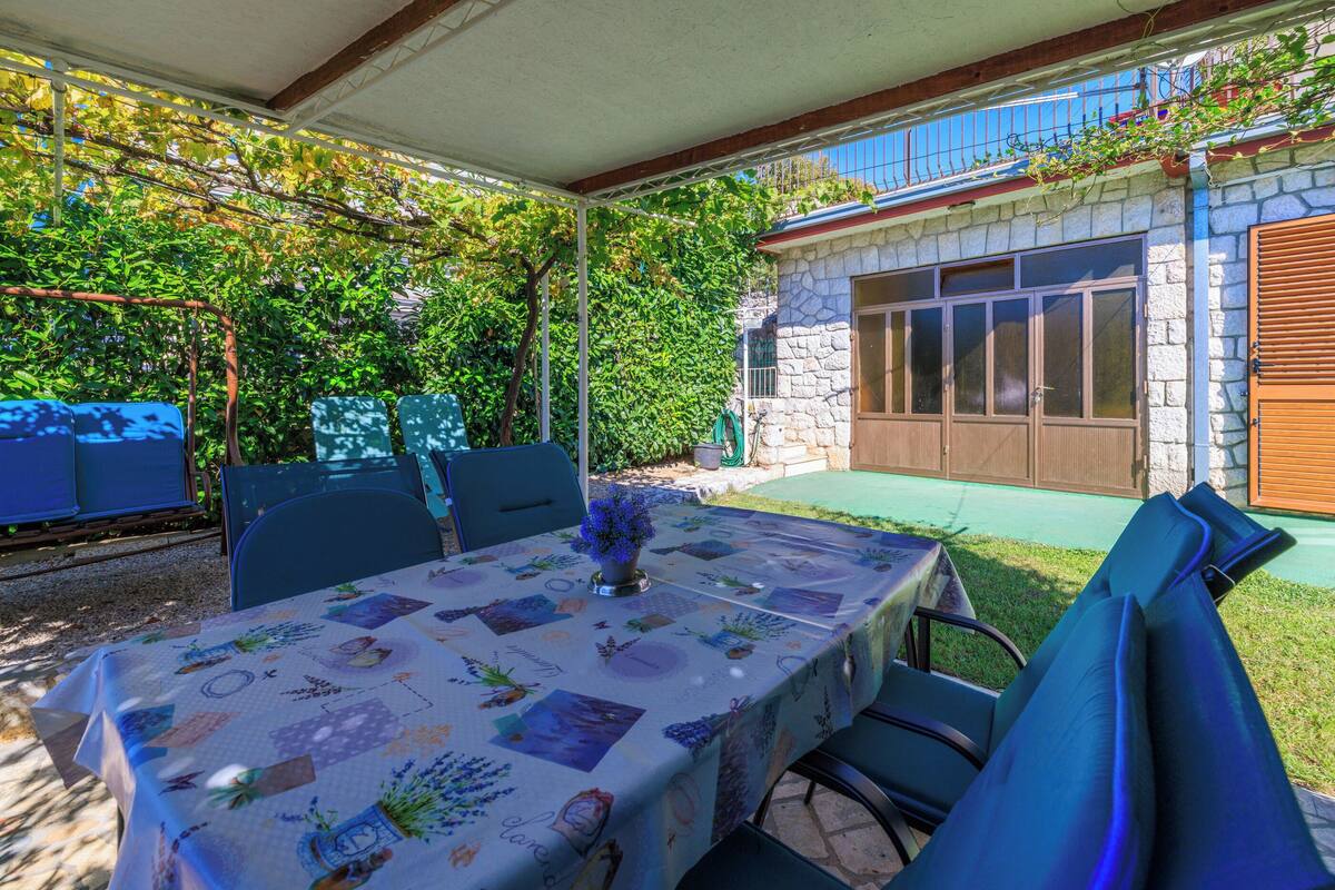 Une terrasse extérieure avec une table dressée pour les repas, entourée de chaises, et un espace salon abrité.