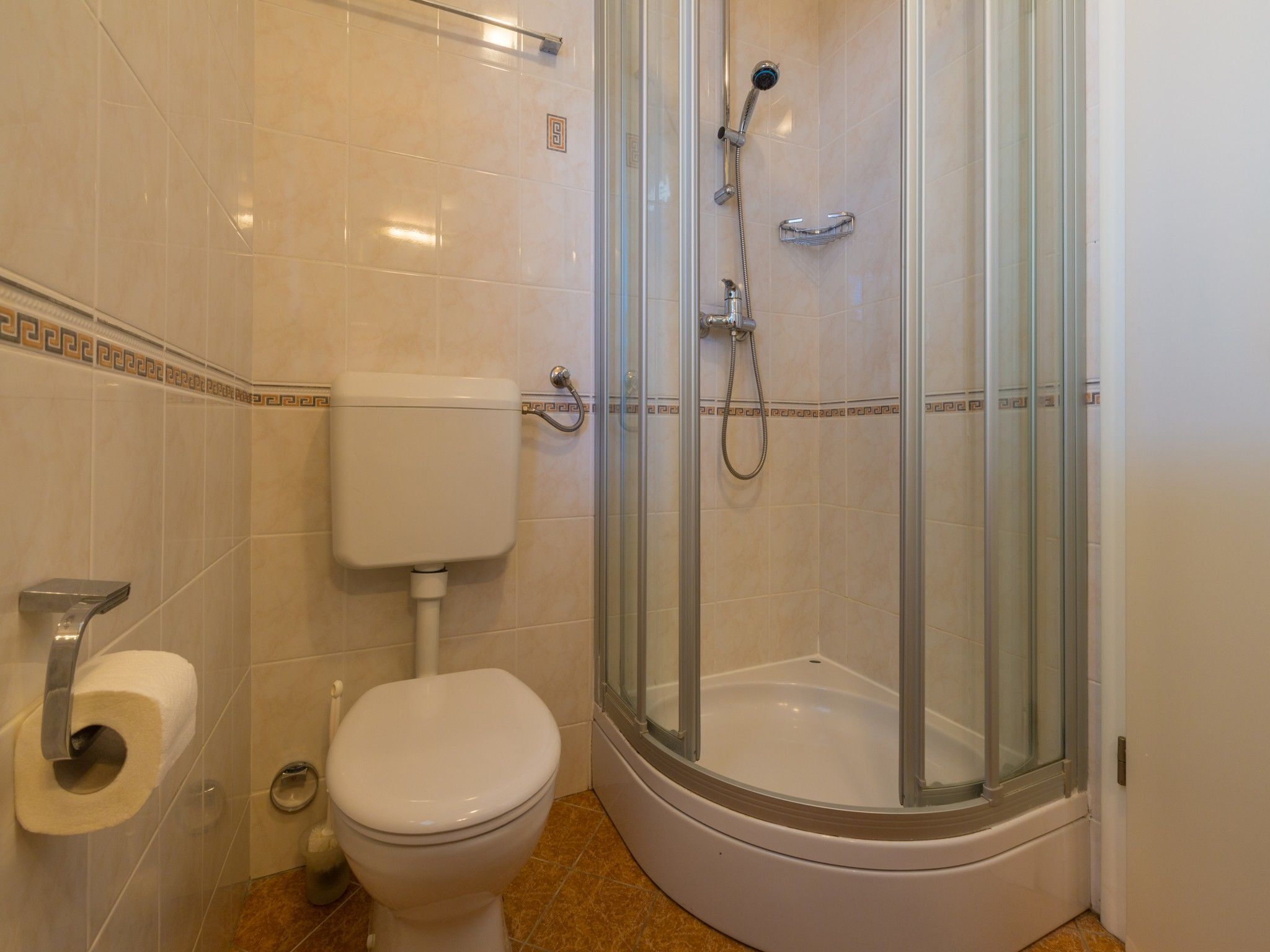 Ein Badezimmer mit Toilette, einer Duschkabine und einem Toilettenpapierhalter.