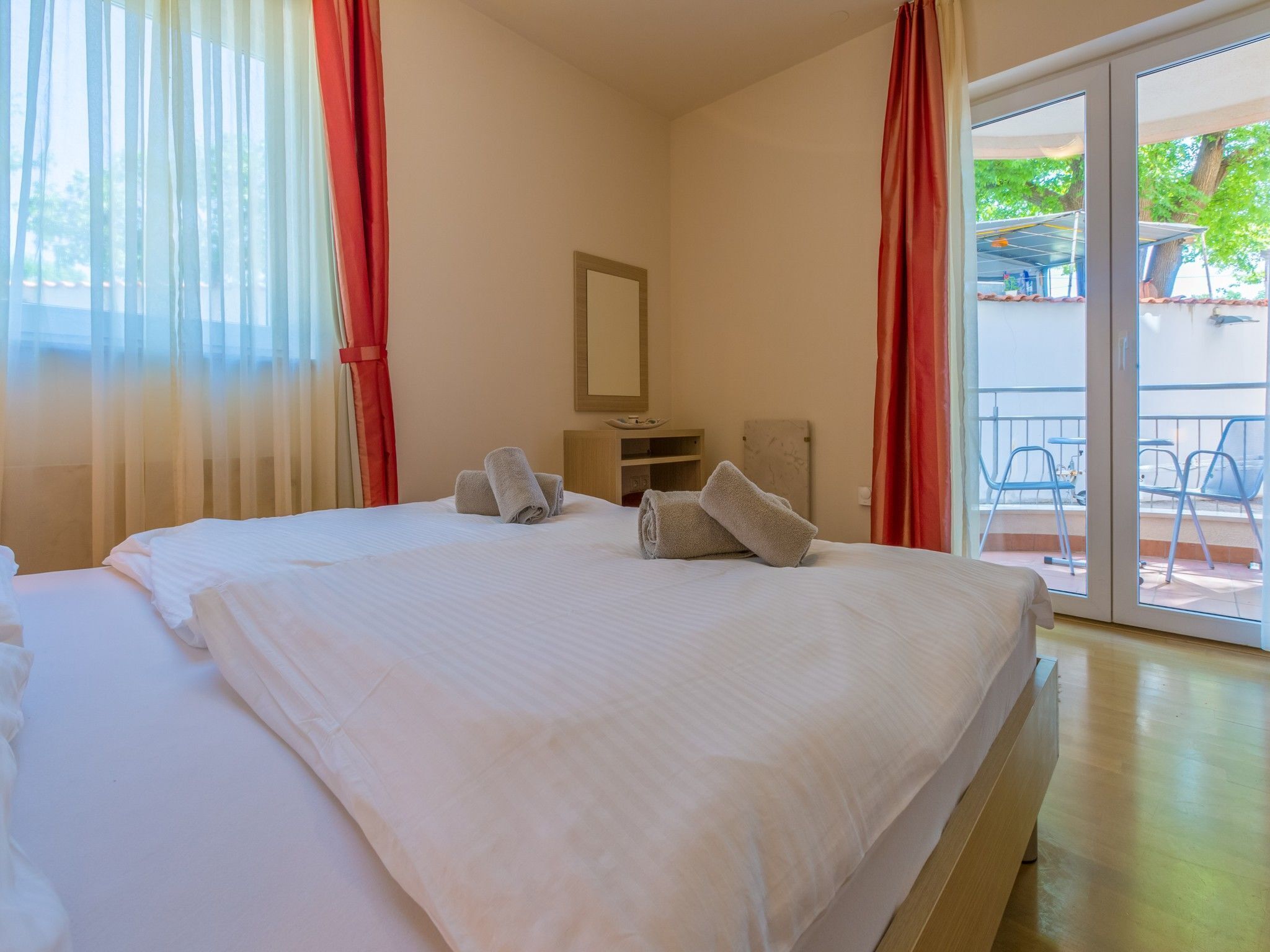 Ein Hotelzimmer mit einem großen Bett, einem kleinen Schreibtisch, einem Spiegel und einem Balkon mit Sitzgelegenheit.
