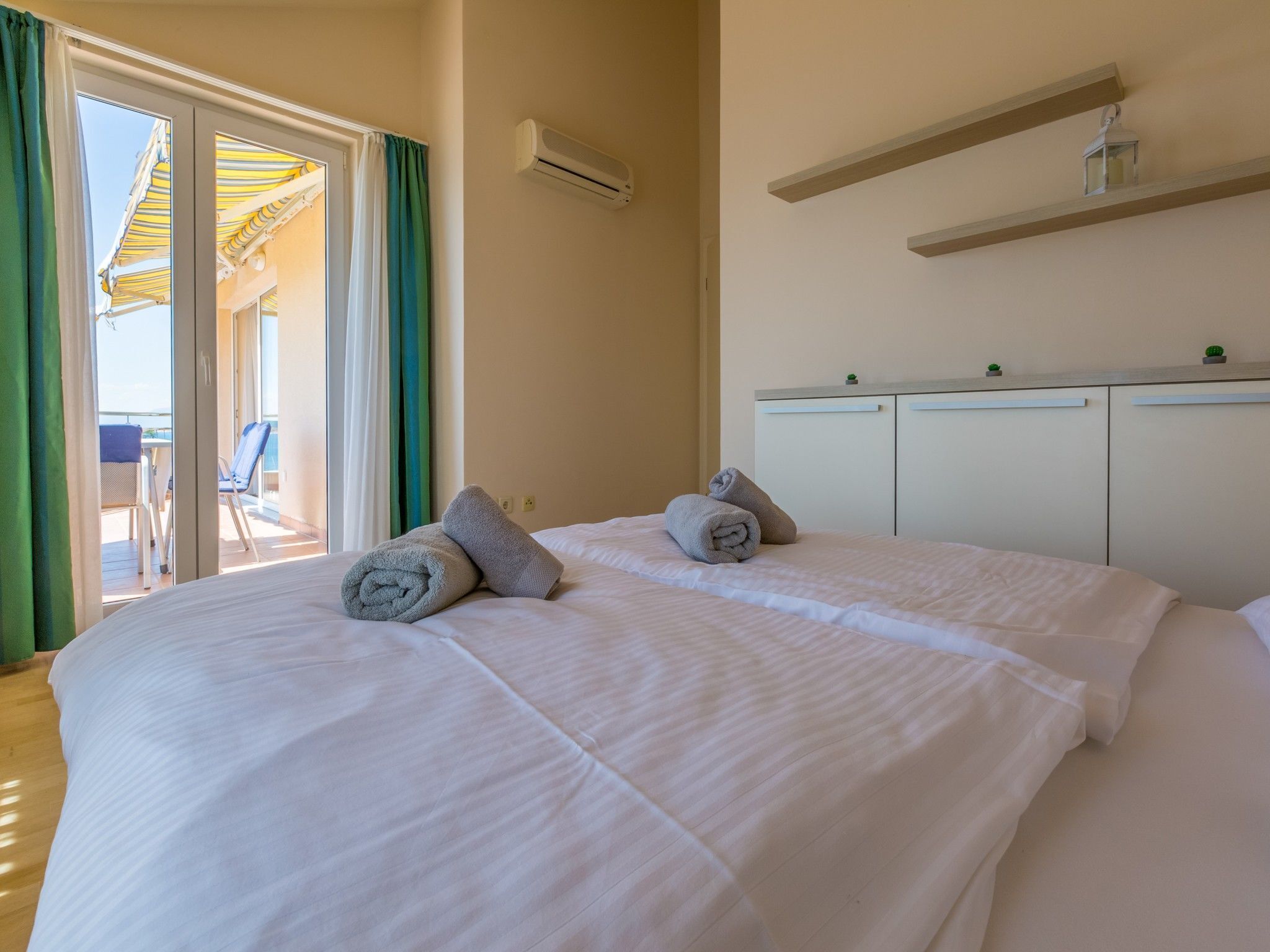 Une chambre d’hôtel avec deux lits, une porte-fenêtre coulissante donnant sur un balcon, une petite table et une armoire blanche.