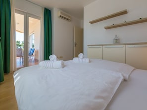 A hotel room with a large bed, two rolled towels, a sliding glass door leading to a balcony, and a small table with a lantern. - Apartments Villa Vanda (Selce)