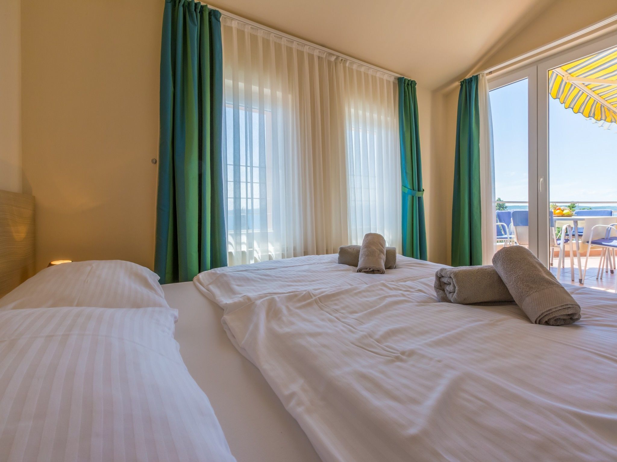 Ein Hotelzimmer mit zwei Betten, einem Balkon mit gelber Markise und Blick aufs Meer.
