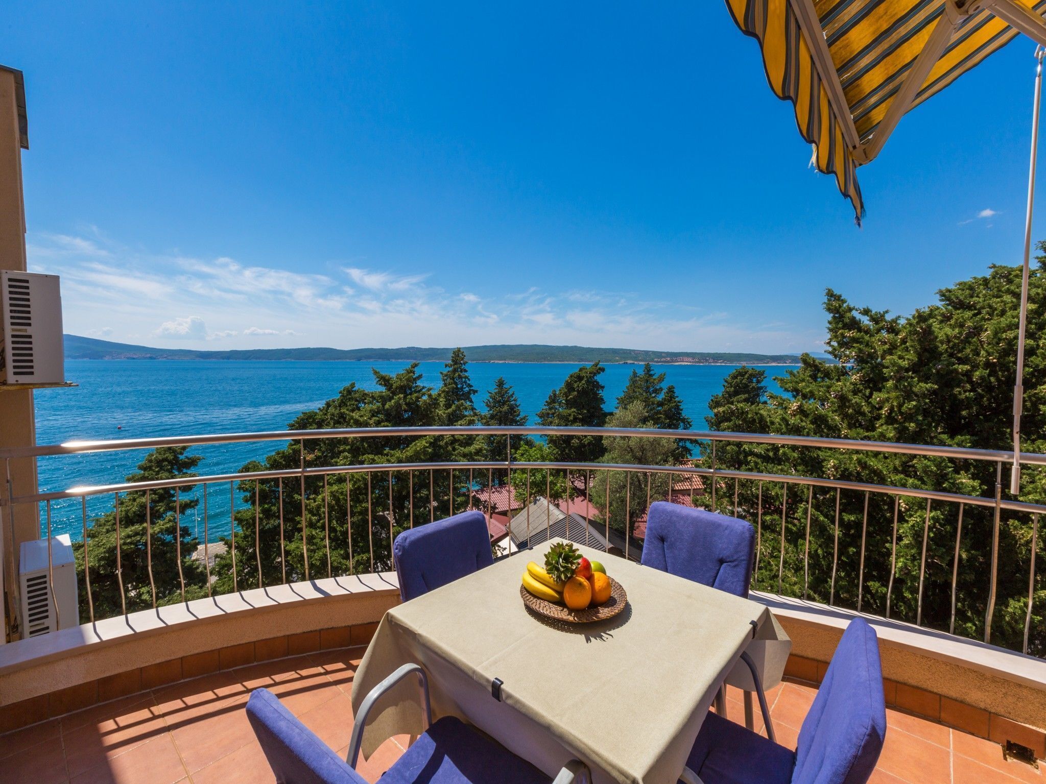 Ein Balkon mit einem Tisch für zwei Personen, mit Blick auf eine malerische Landschaft aus Meer und Hügeln.