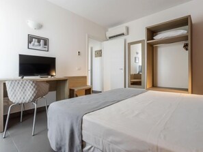 Una camera d'albergo con un letto, una scrivania con una sedia, una televisione e un armadio.