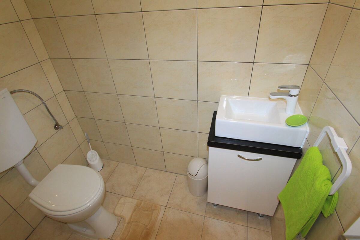 Egy kis fürdőszoba, amelyben WC, mosdókagyló és zuhanyzó található.