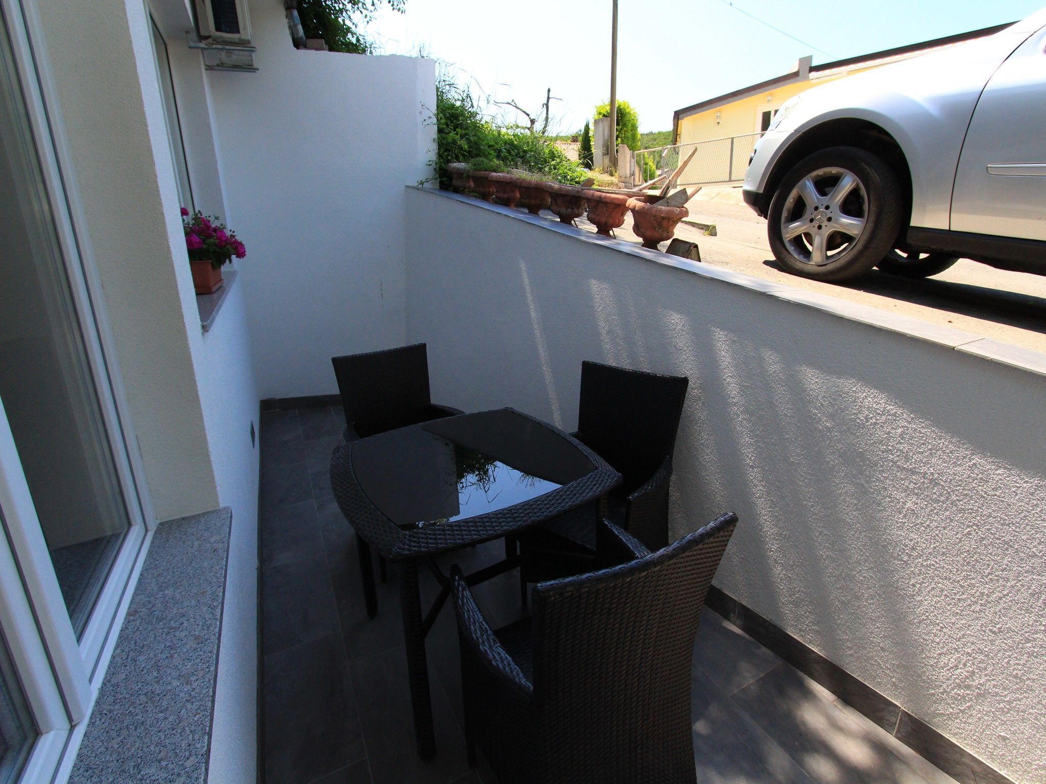 An outdoor patio with a table and chairs, a white wall, and a parked car.