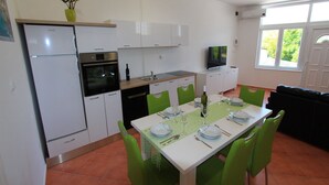 Eine kompakte Küche mit weißen Schränken, einem eingebauten Backofen und einer Essecke mit Tisch für vier Personen.