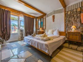 A bedroom with a bed, a stone wall, a wooden headboard, a nightstand, and a window with curtains.