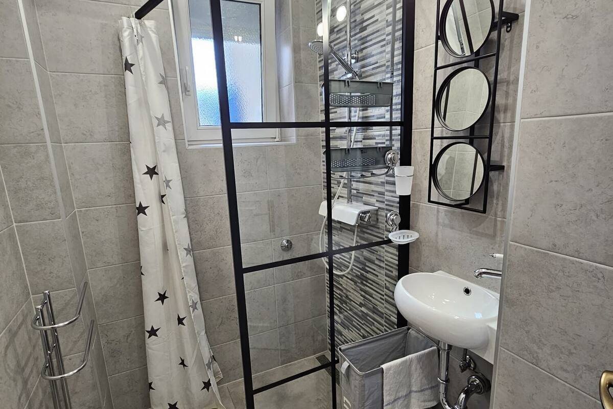 A modern bathroom with a glass shower enclosure, a sink, and a mirror with multiple round mirrors.