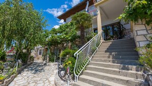 Ένα μονοπάτι στρωμένο με πέτρες, που οδηγεί σε ένα κτίριο με μια μεταλλική σκάλα και ένα μπαλκόνι.