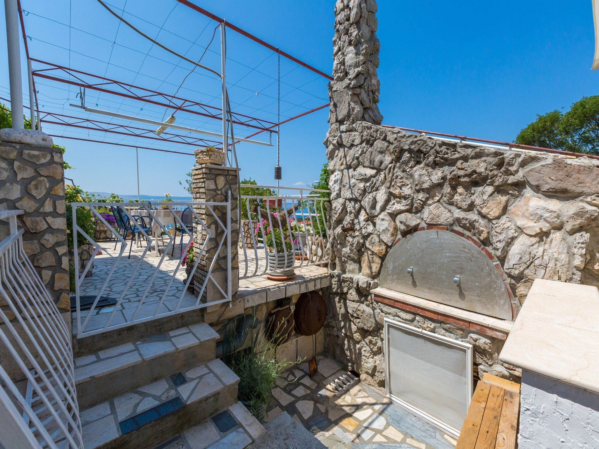 Un espace extérieur entouré de murs en pierre, doté d’un barbecue, d’un escalier menant à une terrasse et offrant une vue sur la mer.