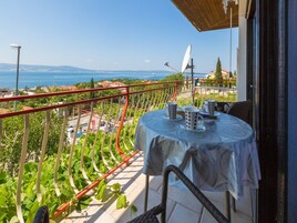 A balcony with a table set for two, overlooking a coastal view.