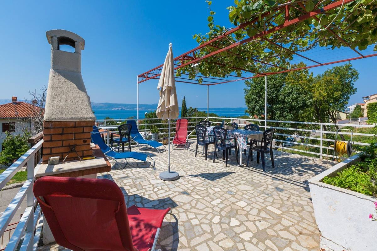 An outdoor patio with stone flooring, red and blue lounge chairs, and a view of the sea.