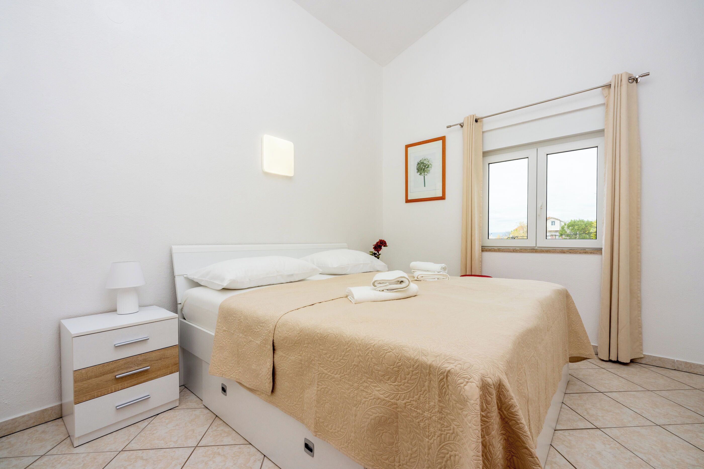 A neatly arranged bedroom with a bed, bedside table, and a window with curtains.