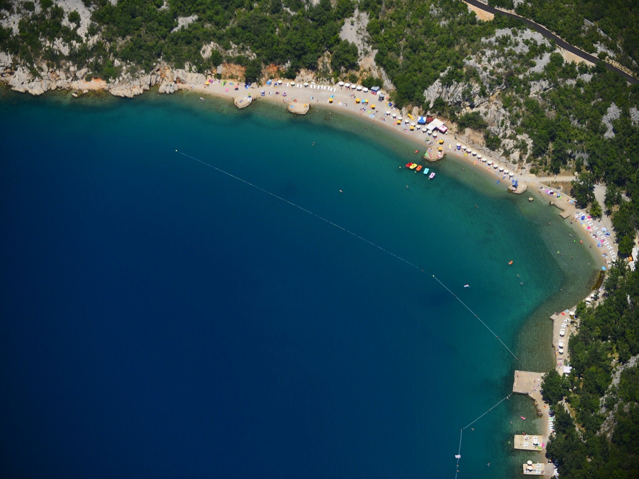 Eine Luftaufnahme einer Küstenregion mit Strand, klarem türkisblauem Wasser und einer felsigen Küstenlinie.
