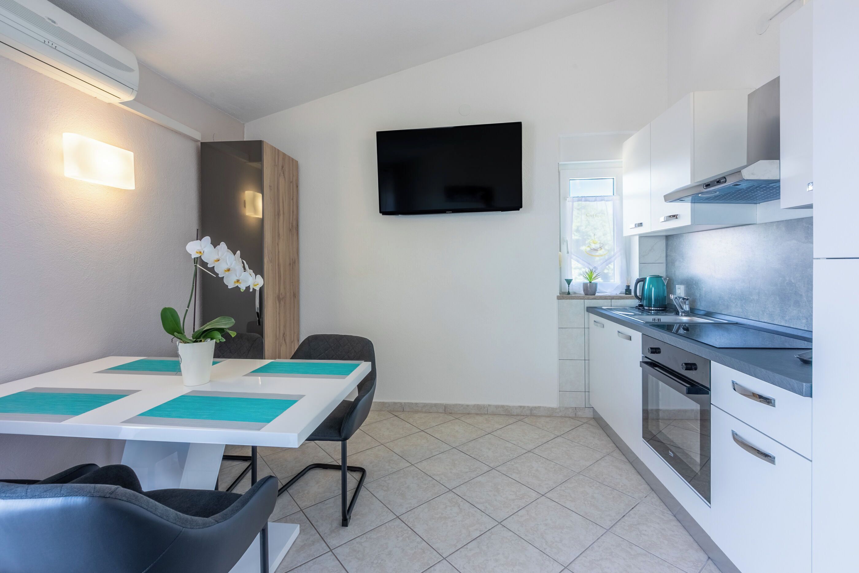 Una cocina moderna con televisor de pantalla plana, armarios blancos y un comedor con mesa y sillas.