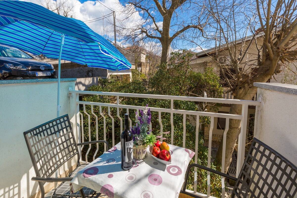 Een balkon met een tafel, stoelen, een fles en een schaal fruit.