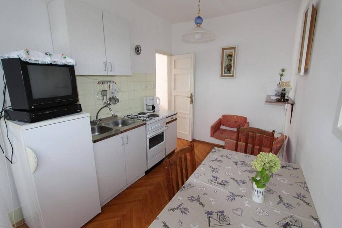 A compact kitchen with a microwave, sink, and stove, a dining table with a floral tablecloth, and a sofa in the background.