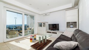 A modern living room with a glass coffee table, a leather sofa, and a flat-screen TV. - Apartment Jana (Crikvenica)