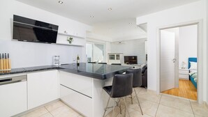 A modern kitchen with a central island, white cabinetry, and a flat-screen TV mounted above the island. - Apartment Jana (Crikvenica)