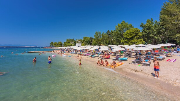 A beach with clear water, umbrellas, and people relaxing. - Apartment Jana (Crikvenica)
