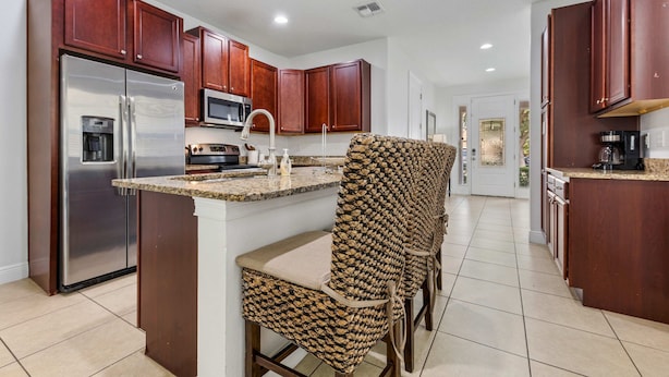 A modern kitchen with dark wooden cabinets, stainless steel appliances, and a central island with bar stools. - 8BR Superb Villa, Pool, Spa • Near Disney (Kissimmee)