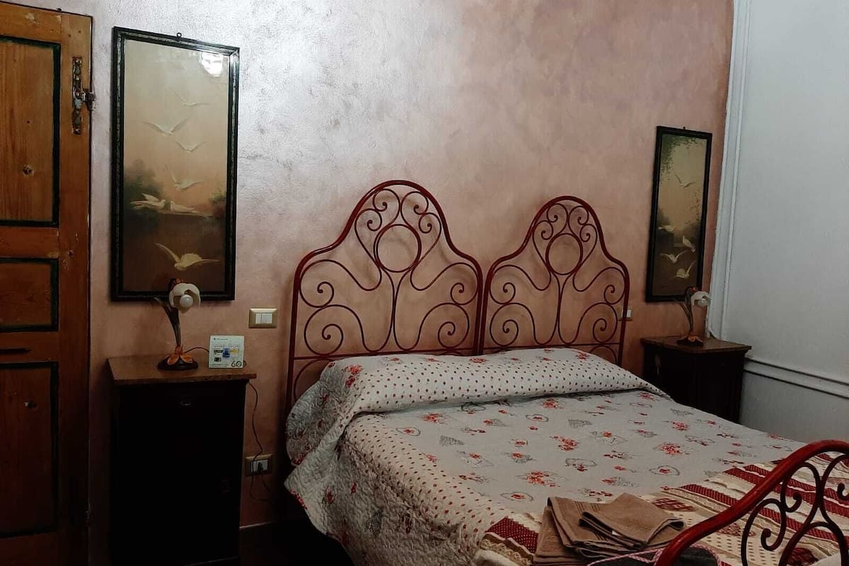 A bedroom with a metal bed frame, a wooden door, and two bedside tables with lamps.