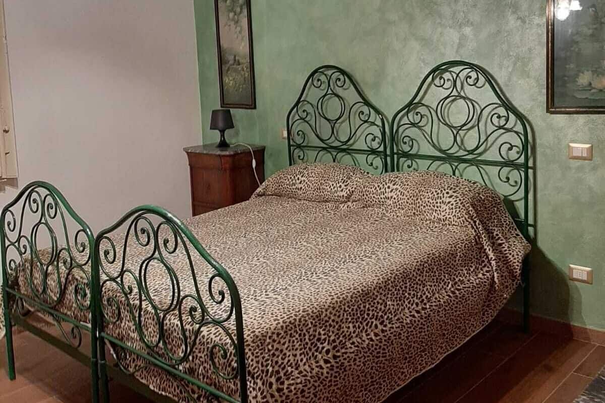 A bedroom with a bed, wooden beams, a green wall, and a chandelier.