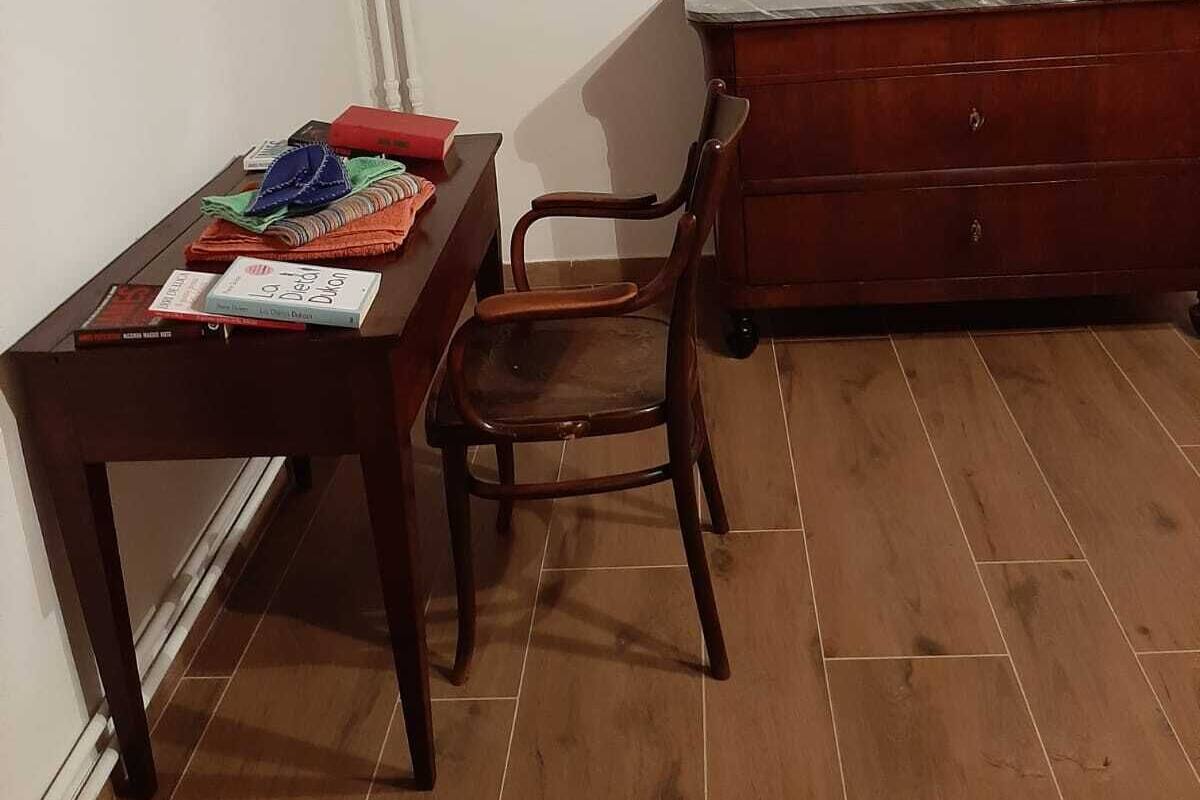 A room with a wooden table, a chair, a dresser, and a framed picture on the wall.