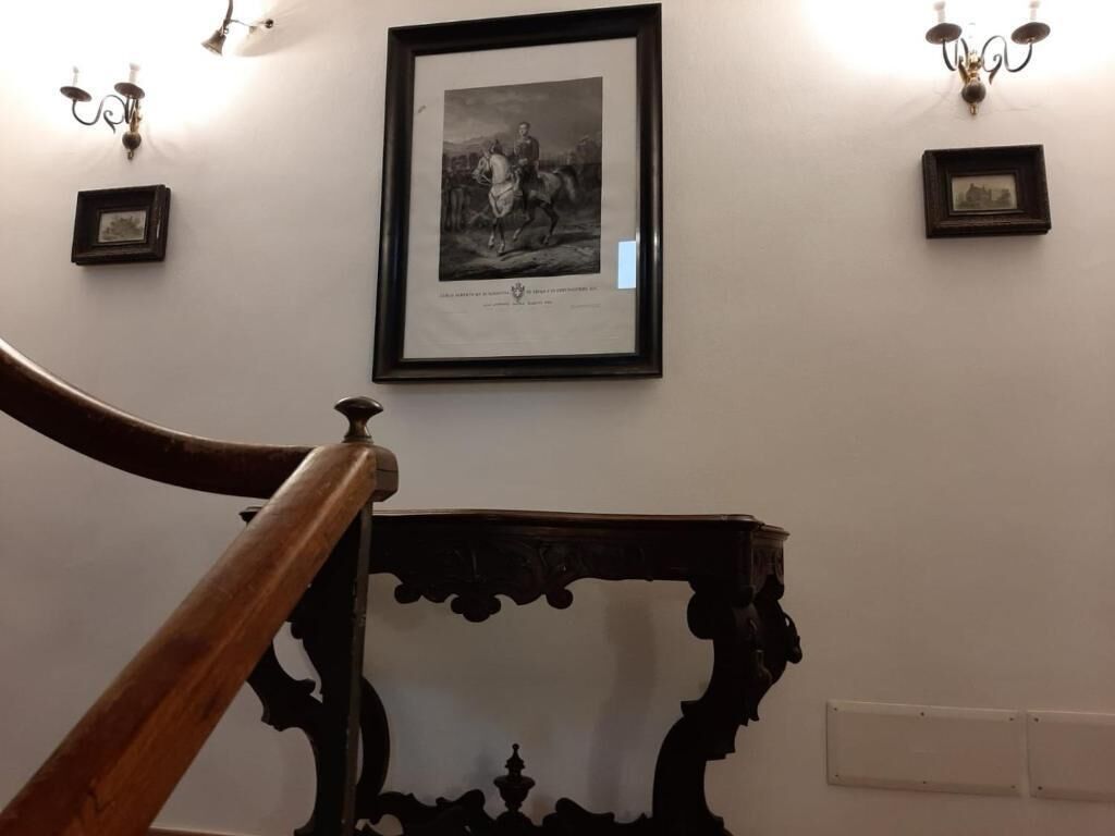 A staircase with a wooden handrail leading to a dark, ornate table against a wall with framed pictures and wall sconces.
