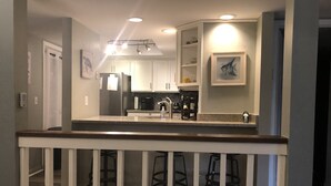 A kitchen with white cabinets, a stainless steel refrigerator, a coffee maker, and a sink. There are two stools under the counter. - 8/27- 9/4  open  5 STARS  Great ratings- Hidden Gem Great Lagoon/Golf/pool view (Hilton Head Island)