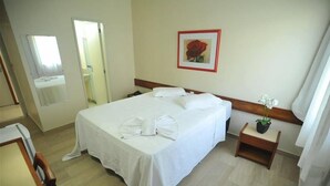 Una habitación de hotel con una cama grande, una mesita de noche con una planta y un cuadro en la pared.