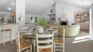 A modern kitchen with a dining area, featuring a glass table, wooden chairs, and a central island with seating. - Limoncello Grove: Brand new Hot Tub in 2025!! Private Pool, Pet-Friendly (Corolla)