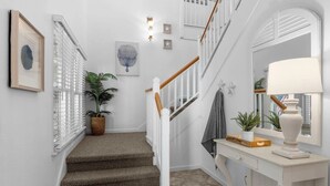 A staircase with a white railing, a potted plant, and a lamp on a white console table. - Limoncello Grove: Brand new Hot Tub in 2025!! Private Pool, Pet-Friendly (Corolla)