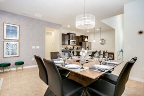 A modern dining area with a wooden table set for six, black chairs, and a chandelier.
