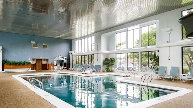 Une piscine intérieure à l’eau claire, entourée de chaises longues et dotée d’un grand mur vitré.