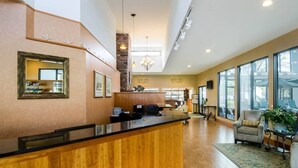 Un hall d’hôtel avec un comptoir d’accueil en bois, des œuvres d’art encadrées et un lustre.