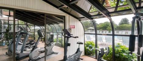 Una palestra con attrezzature per esercizi, tra cui tapis roulant e macchinari per pesi, e vista su un'area relax all'aperto e vegetazione attraverso ampie vetrate.