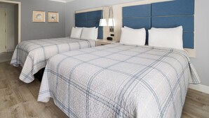 Une chambre d’hôtel avec deux lits, une tête de lit ornée d’un panneau bleu, une table de chevet avec une lampe et des œuvres d’art encadrées accrochées au mur.
