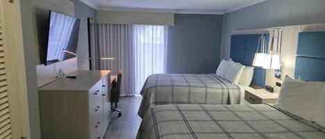 A hotel room with two beds, a desk with a chair, a TV, and a window with curtains.