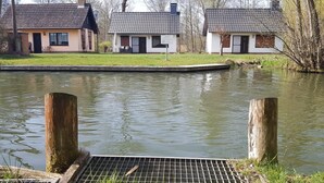 Ruhige Wasserfläche mit hölzernen Pfählen und einem Metallgitter.
