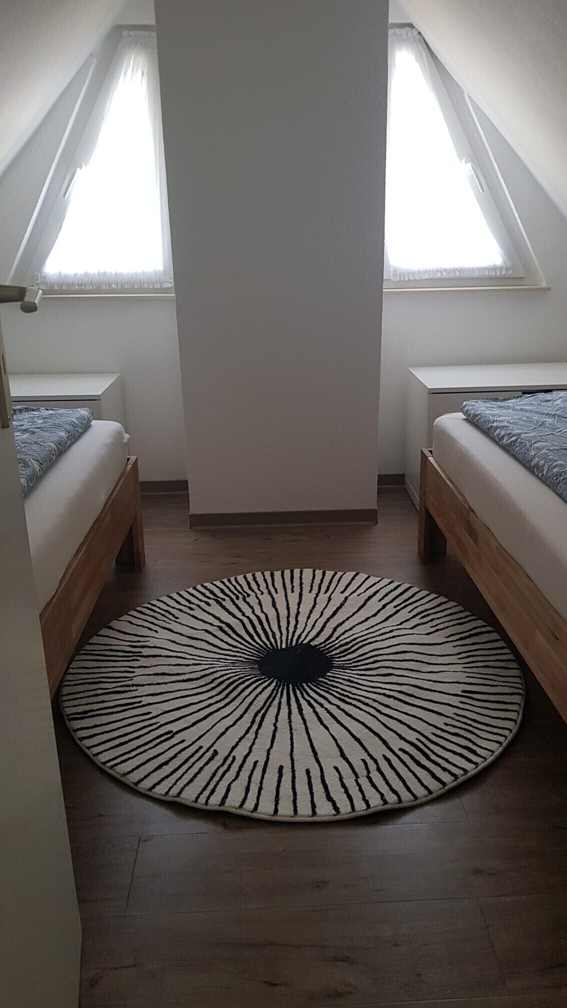 A small, well-lit room with a round zebra-patterned rug, two wooden beds, and a white ceiling.