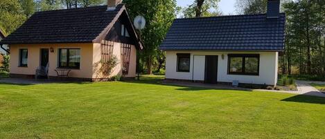 Two houses with distinct architectural styles, one with a sloped roof and the other with a flat roof, both surrounded by a well-maintained lawn.