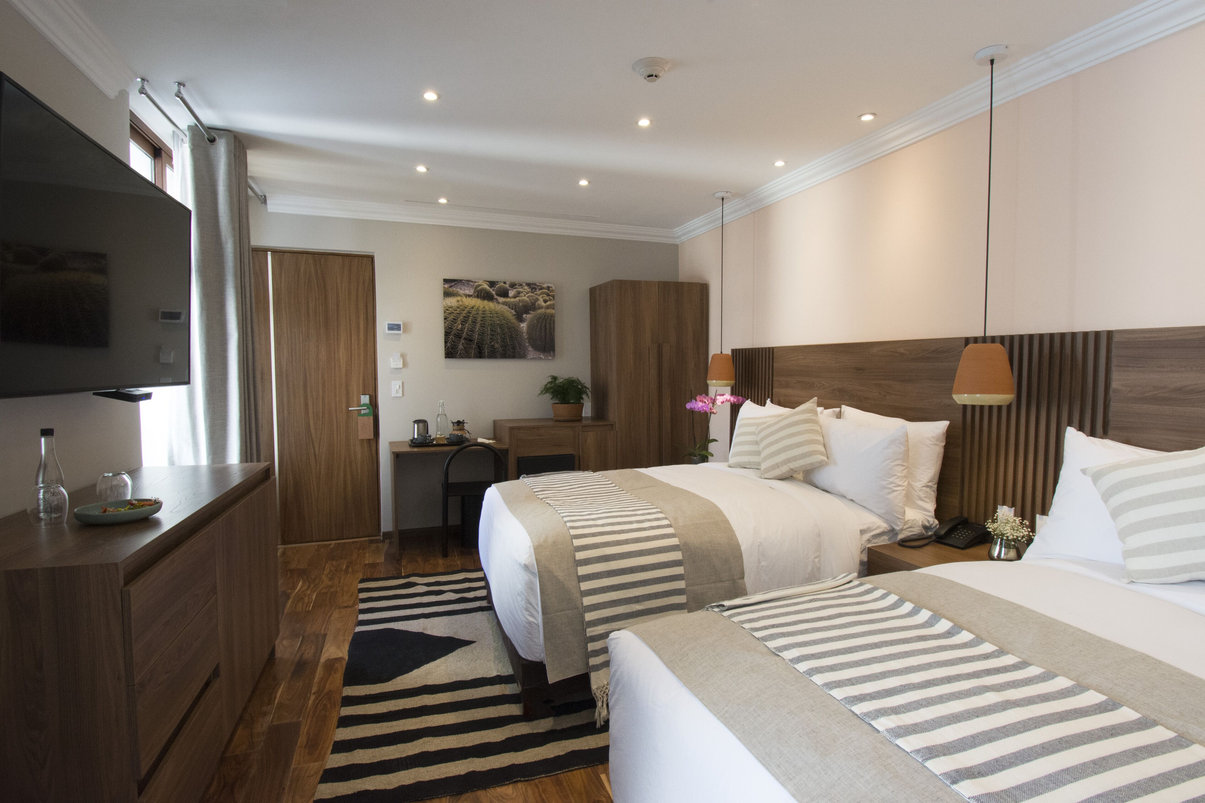 A hotel room with two beds, a desk, a TV, and a wooden wardrobe.