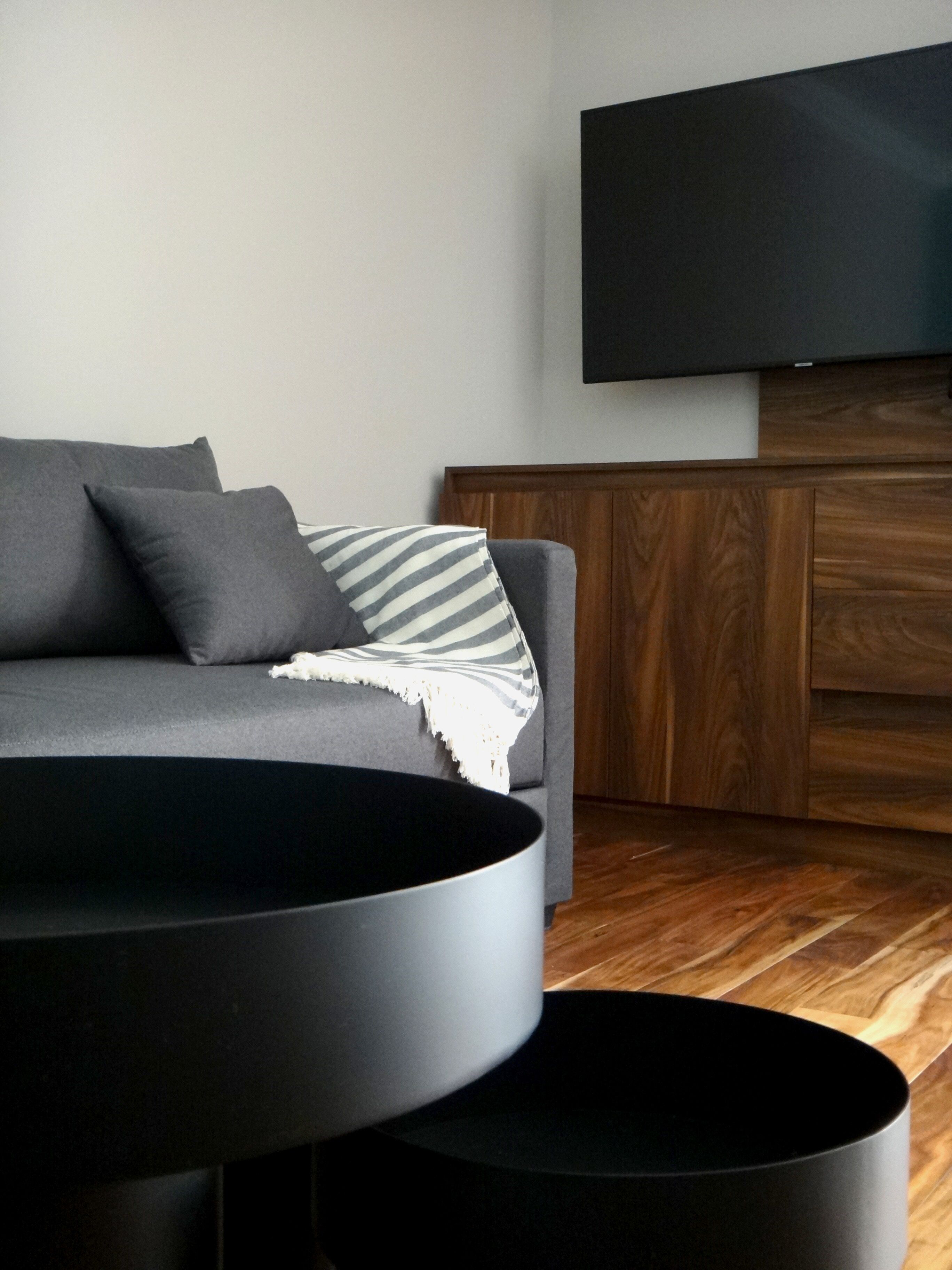 Een moderne woonkamer met een grijze bank, een gestreepte plaid en een flatscreen televisie bevestigd aan een houten wand.