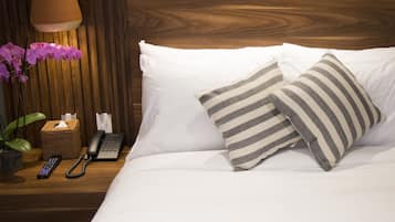 Una cama bien hecha con almohadillas a rayas, una mesita de noche con un teléfono, una lámpara y una planta en maceta.
