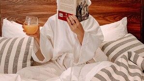 Une personne est assise dans son lit, en train de lire un livre, avec un oreiller à rayures et une tête de lit en bois.