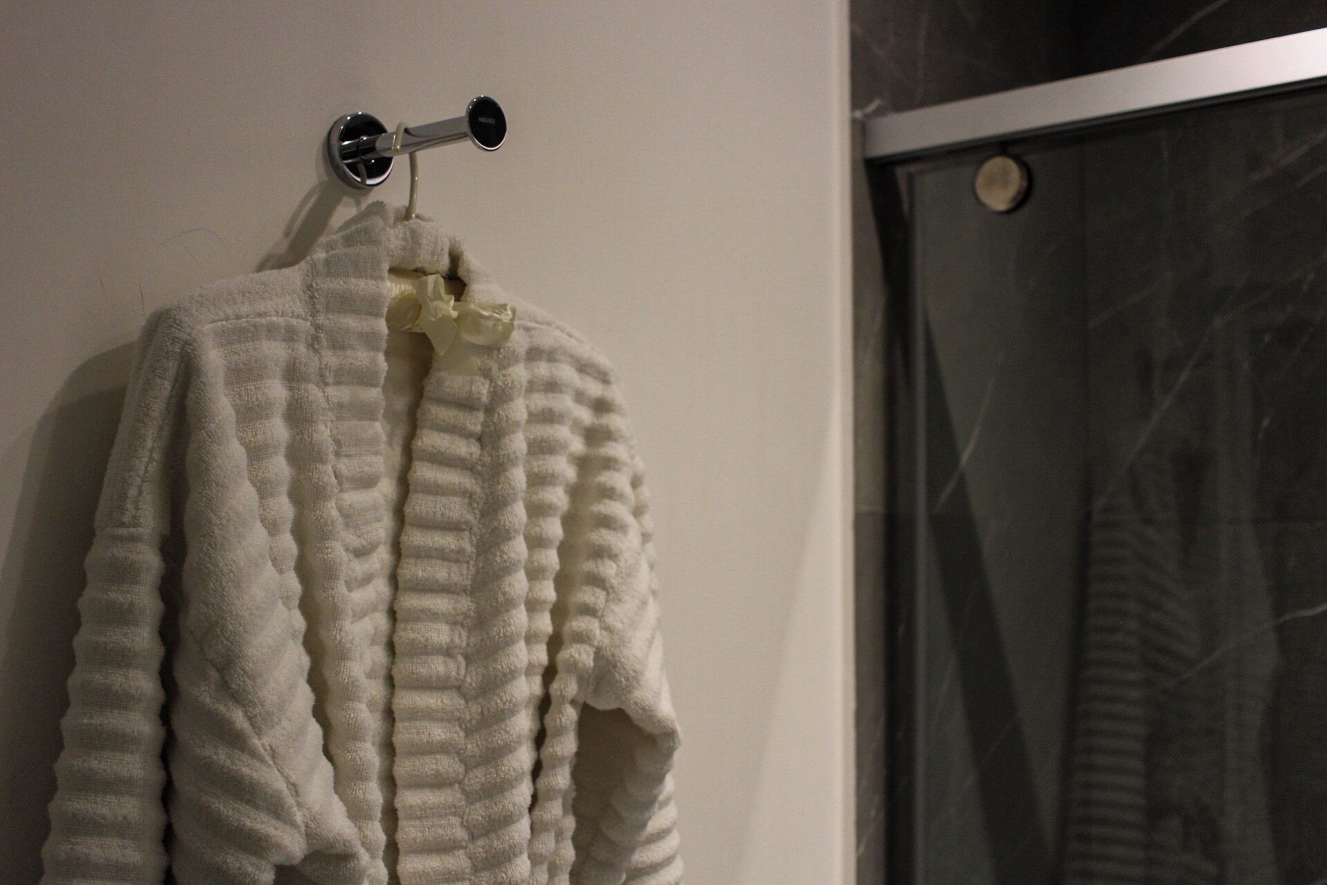 Une serviette blanche est suspendue à un porte-serviettes en métal dans une salle de bain dotée d’une porte de douche en verre.