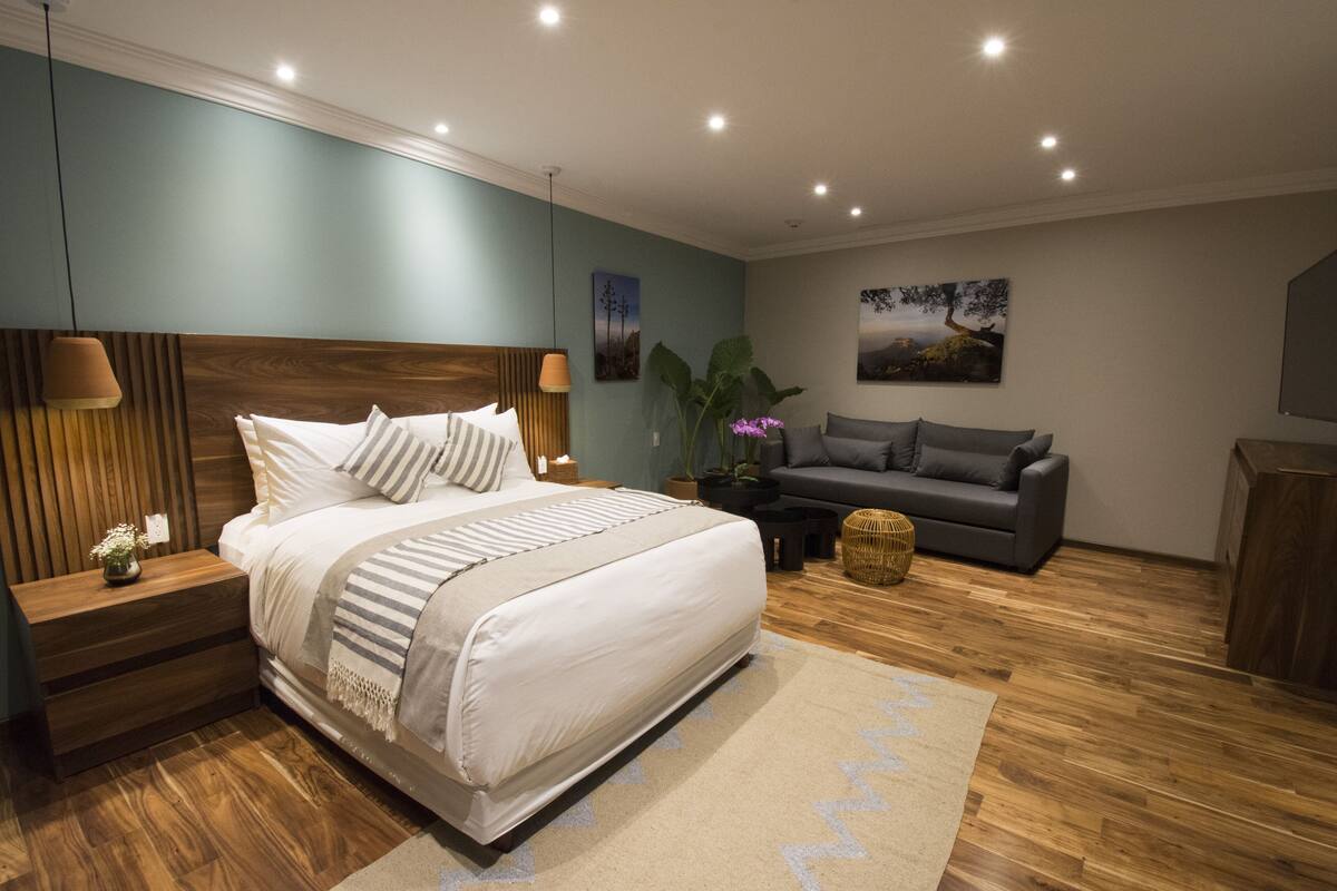 Une chambre à coucher avec un grand lit, des tables de chevet, un canapé gris et un plancher en bois.